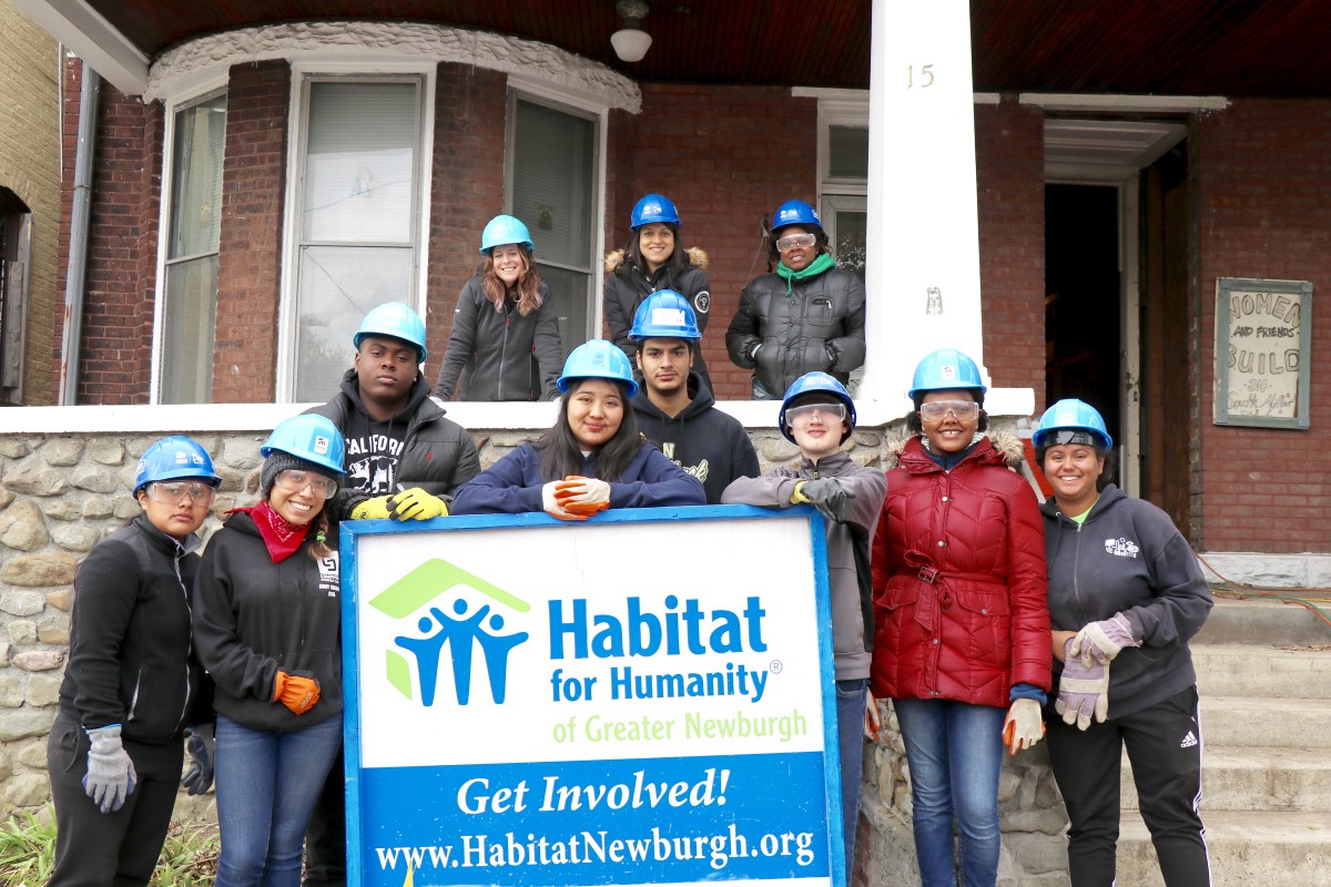 Students pose in front of house and Habitat sign