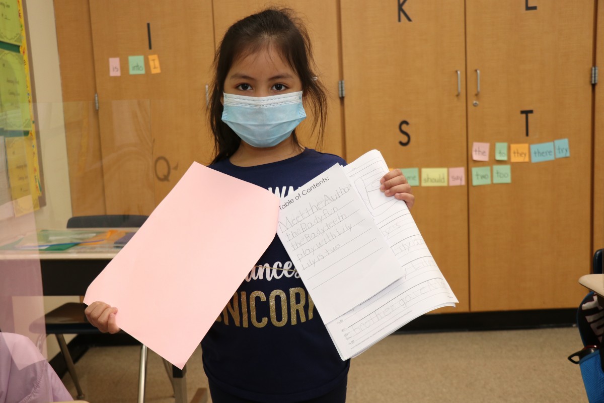 Scholar holding up the book that they wrote, illustrated, published, and read.