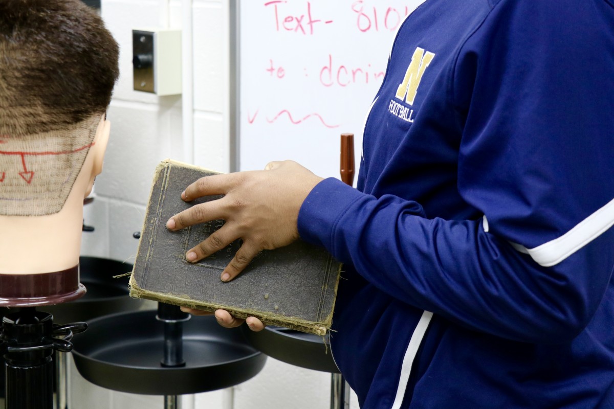 Students hold first barbering book from 1927