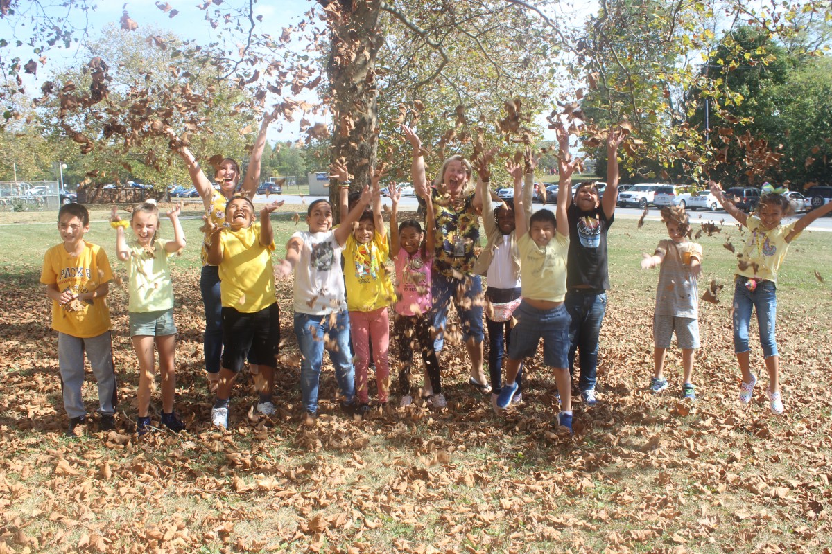 Students wearing gold toss gold leaves in the air.