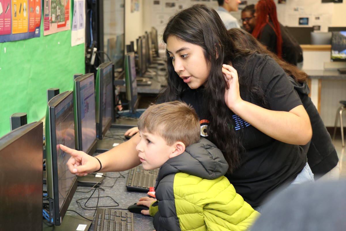 High school scholar helps younger student with coding activity.