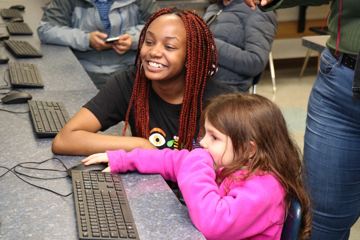 High school scholar helps younger student with coding activity.