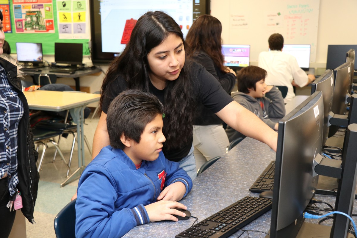 High school scholar helps younger student with coding activity.