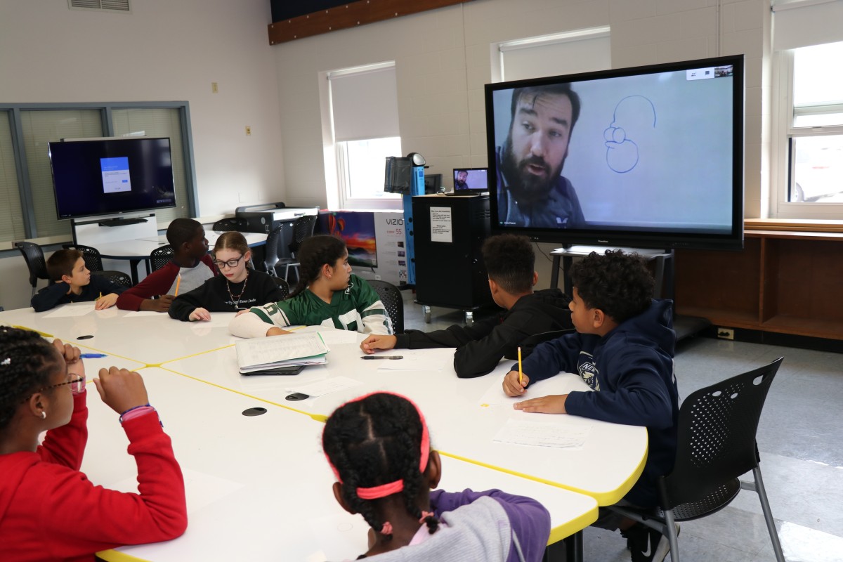 Students try drawing characters using a handful of shapes, under the direction of the presenter.