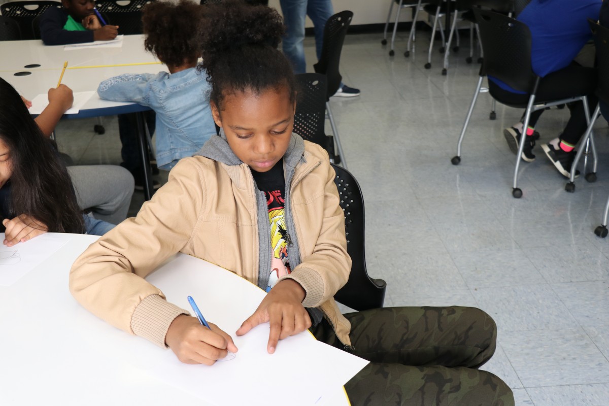 Students try drawing characters using a handful of shapes, under the direction of the presenter.