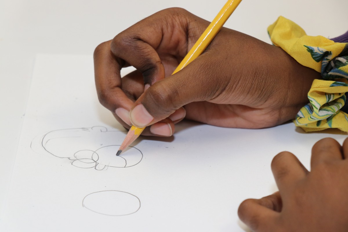 Students try drawing characters using a handful of shapes, under the direction of the presenter.