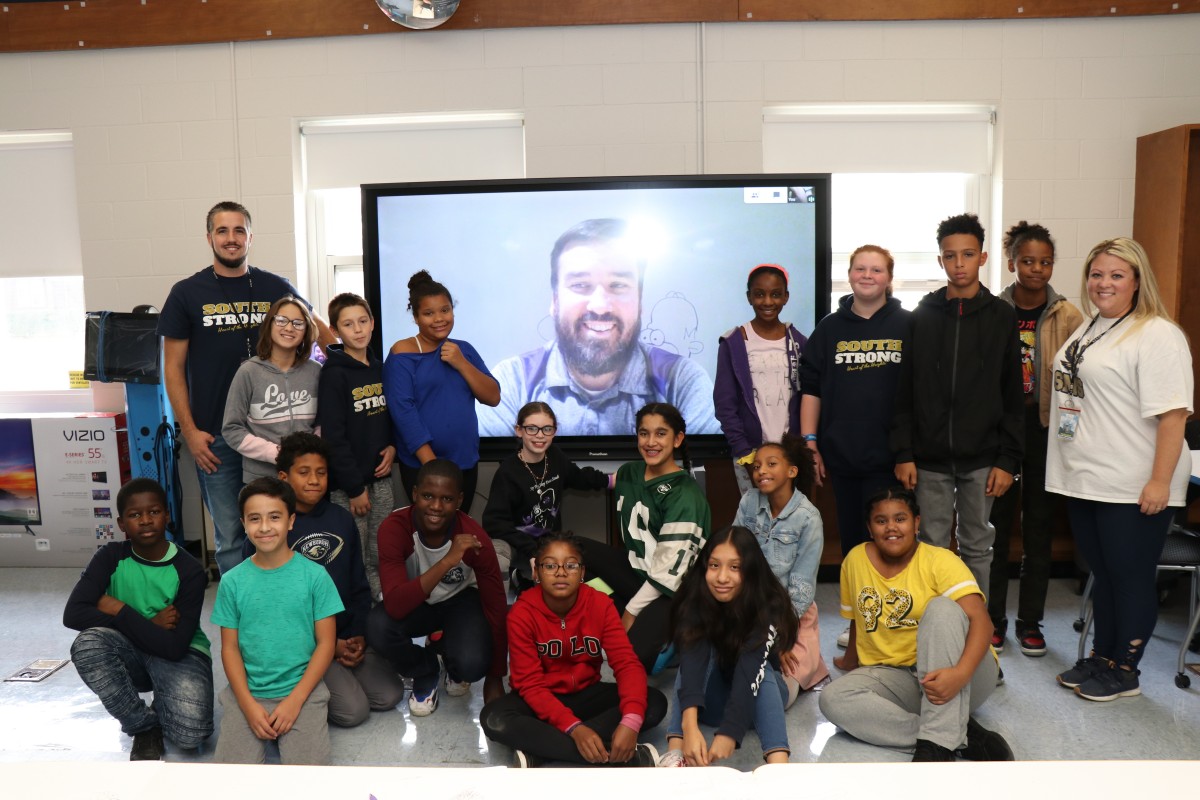 Class poses for a picture with presenter on Promethean board.