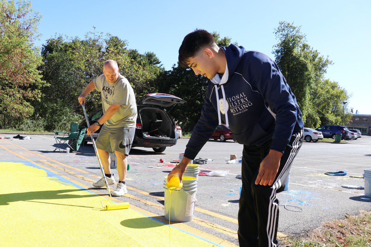 Student and helper painting parking spot.
