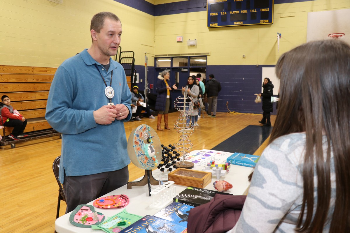 8th grade scholars and their families receive information at a table.