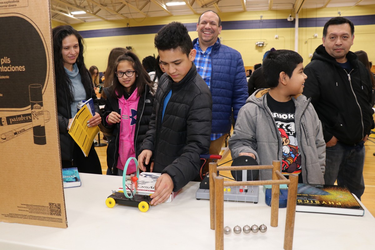 8th grade scholars and their families receive information at a table.