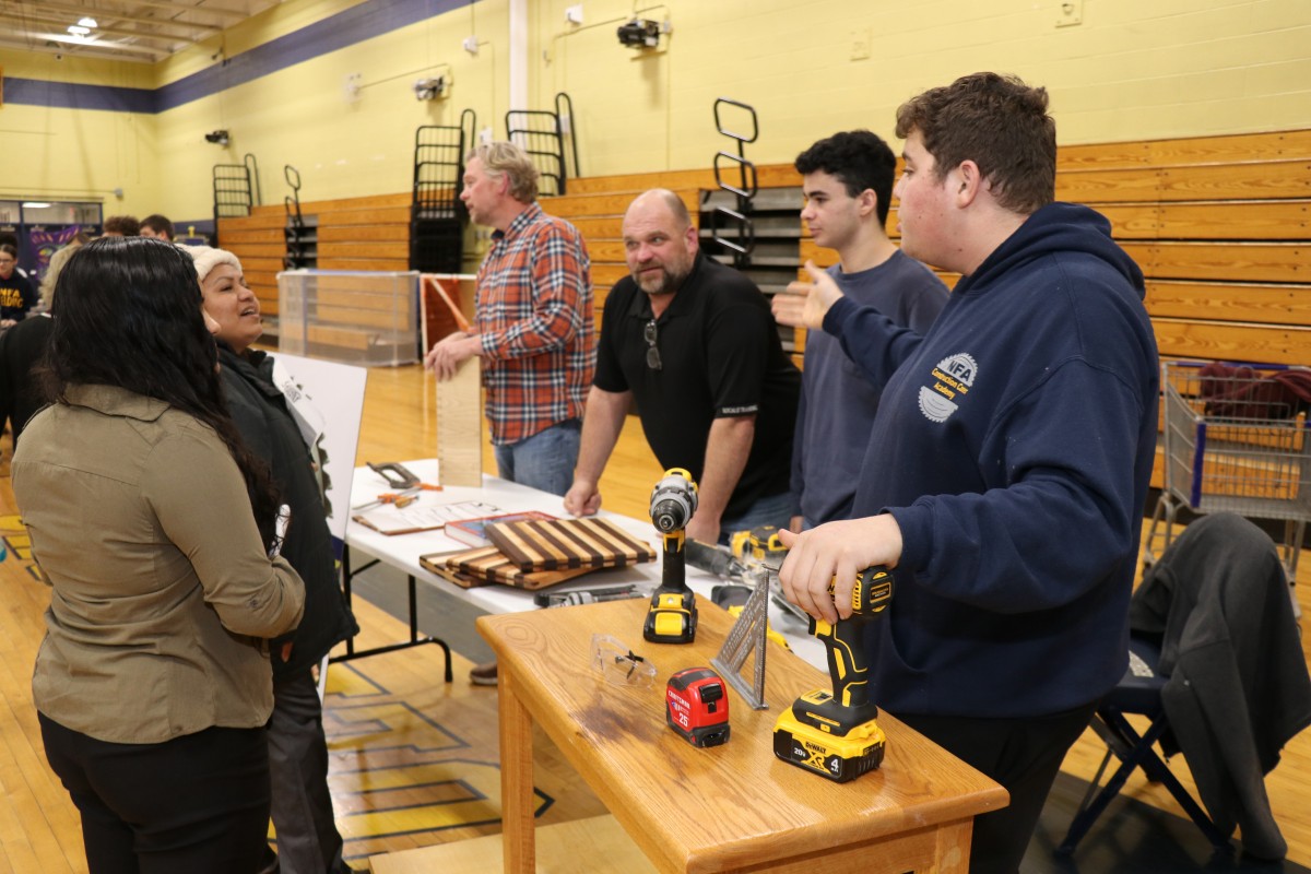 8th grade scholars and their families receive information at a table.