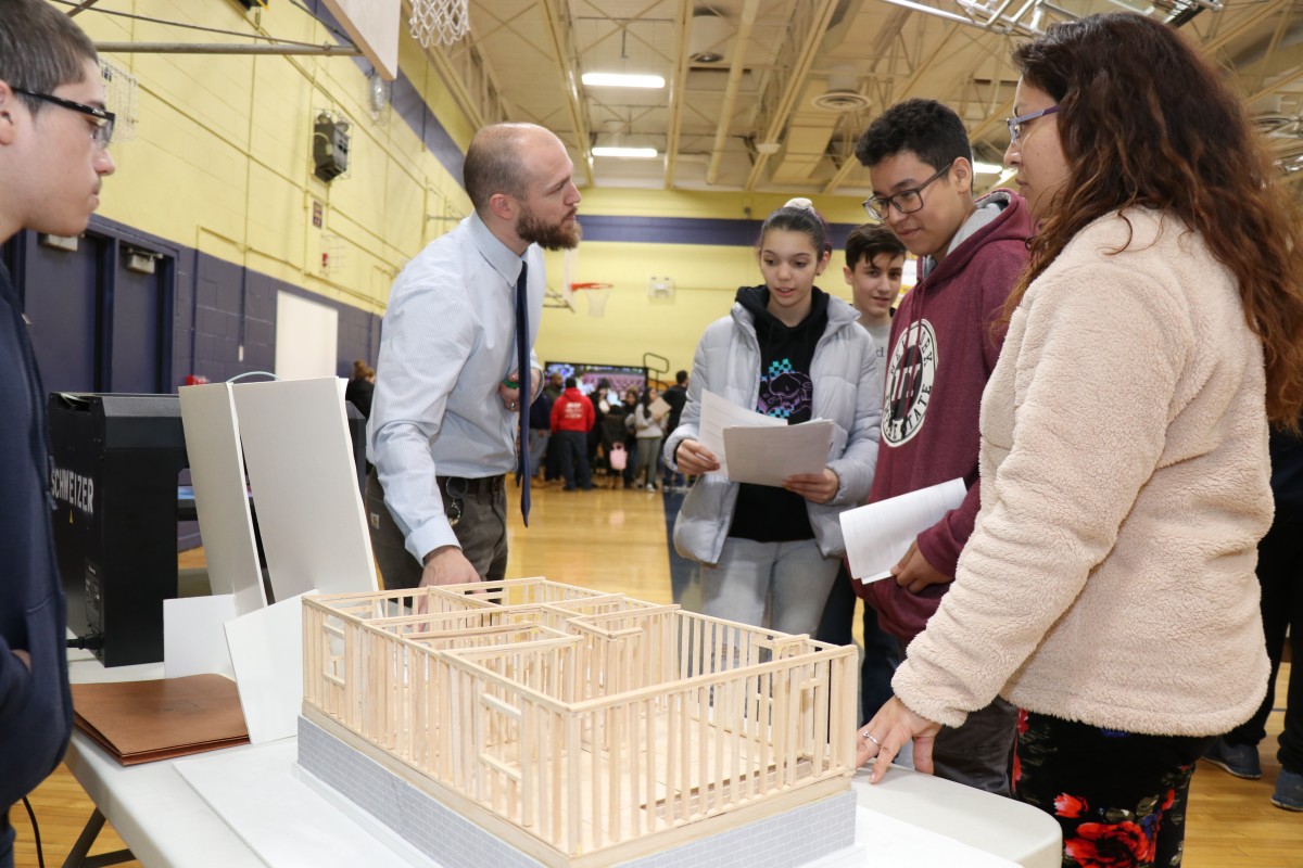 8th grade scholars and their families receive information at a table.