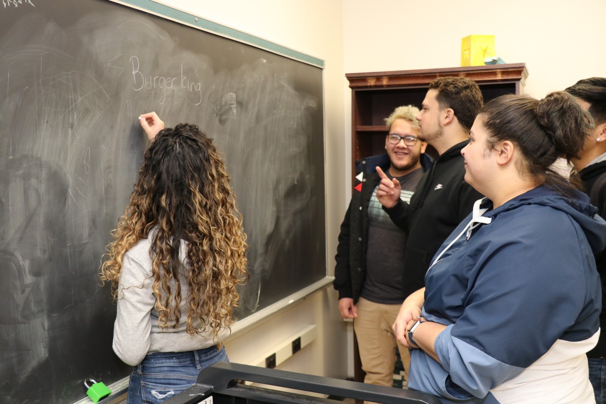 Student writing list on chalkboard.