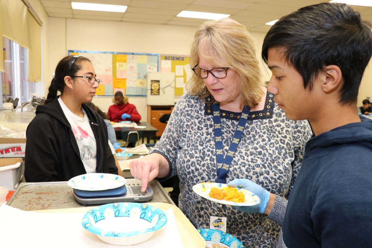 Teacher assisting student weighing pumpkin contents.