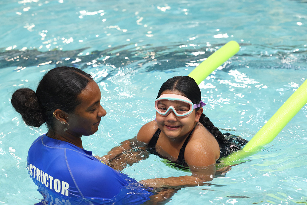 A swim instructor works with a child wearing swim goggles in a pool.