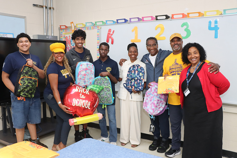 Students and adults pose with backpacks and school supplies inside a classroom.